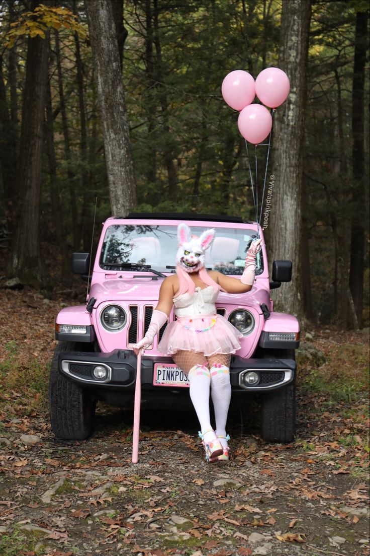 a woman dressed as a bunny sitting in front of a pink jeep with balloons attached to it