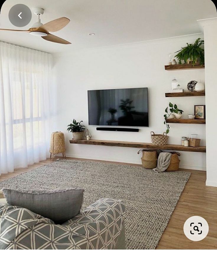 a flat screen tv sitting on top of a wooden shelf in a living room next to a window