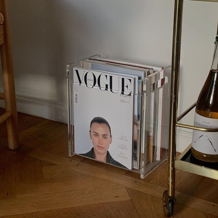 a magazine rack sitting on top of a hard wood floor next to a bottle of wine