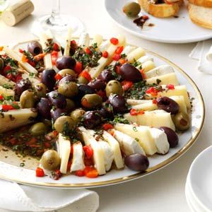 a platter filled with olives and cheese on top of a white table cloth