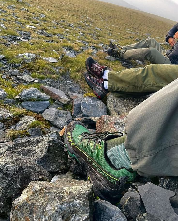 two people sitting on some rocks with their feet in the air and one person wearing hiking boots