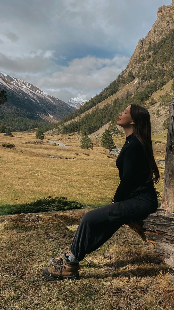 a woman is sitting on a log in the mountains