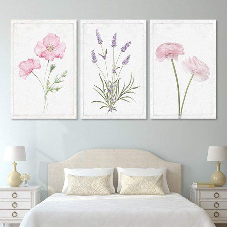 three pink flowers are displayed on the wall above a bed with white sheets and pillows