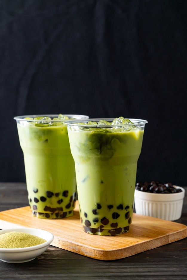 two glasses filled with green smoothie sitting on top of a wooden cutting board