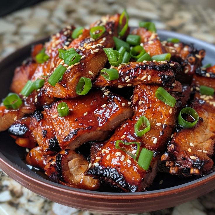 a brown bowl filled with meat covered in sesame seeds and green onions on top of a table