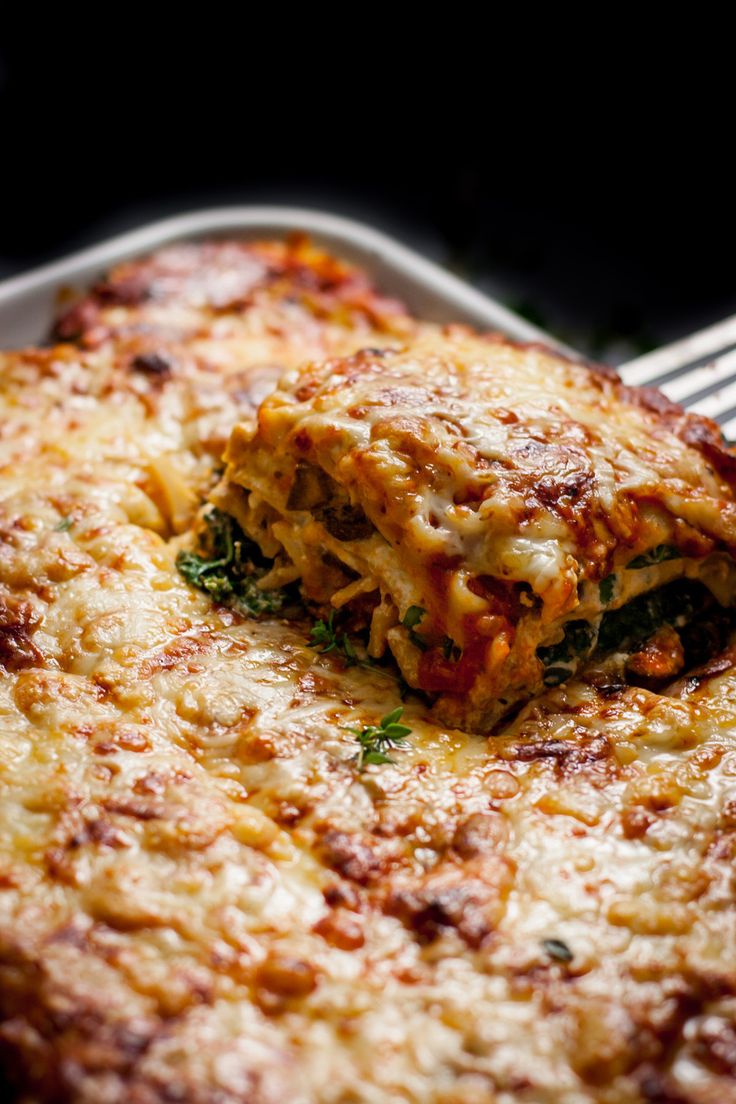 a piece of lasagna on a plate with a fork and knife in the foreground