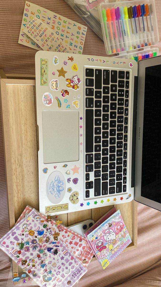 an open laptop computer sitting on top of a wooden desk covered in stickers and magnets