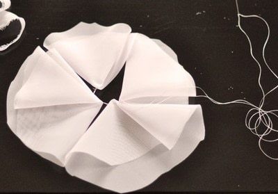 scissors, thread and white paper on a black table with an origami flower