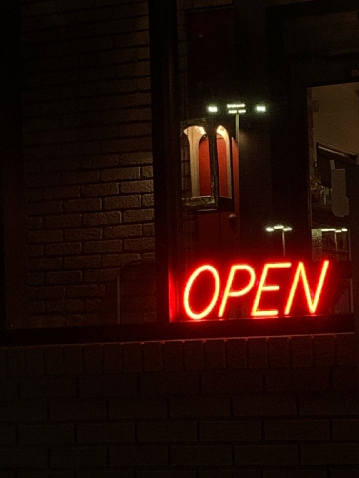 an open sign lit up on the side of a brick building at night with red lights