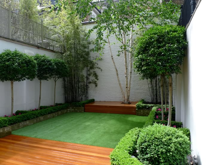 a small backyard with wooden decking and green grass area in the center, surrounded by trees