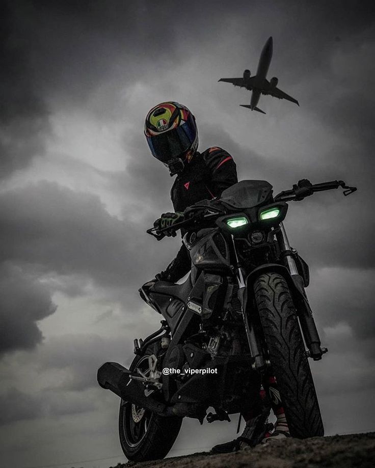 a man riding on the back of a motorcycle under a dark sky with an airplane in the background