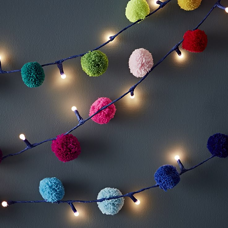 multicolored pom - poms are strung on a string with fairy lights