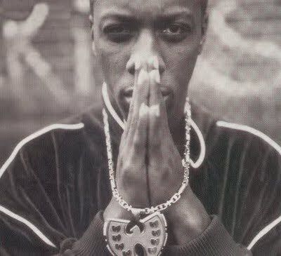 a black and white photo of a man with his hands clasped to his face while wearing a chain around his neck