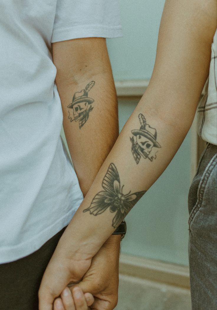 two people holding hands with tattoos on their arms