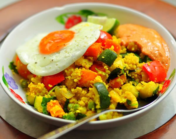 a white bowl filled with vegetables and eggs on top of a wooden table next to a fork