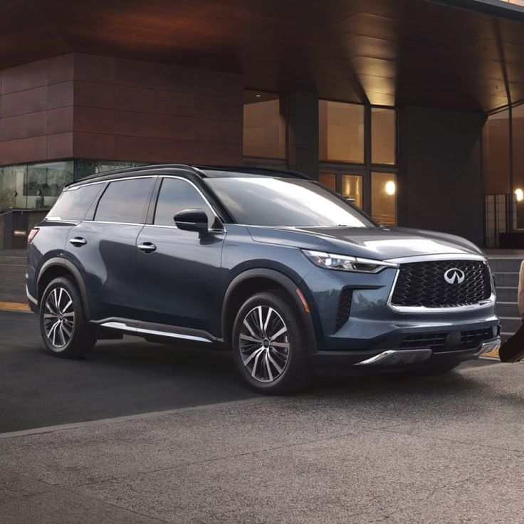 the new infiniti suv is parked next to an older model car outside a building