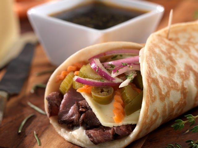 a burrito filled with meat and vegetables next to a bowl of dipping sauce on a cutting board