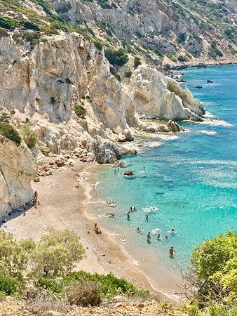 people are swimming in the blue water near some cliffs