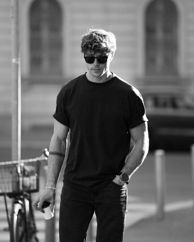 a man in black shirt and sunglasses standing next to a bike on the side walk