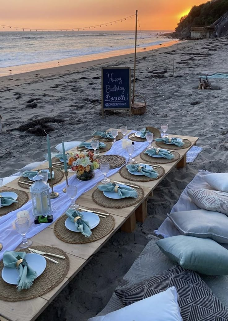 a long table set up on the beach with plates and napkins laid out in front of it