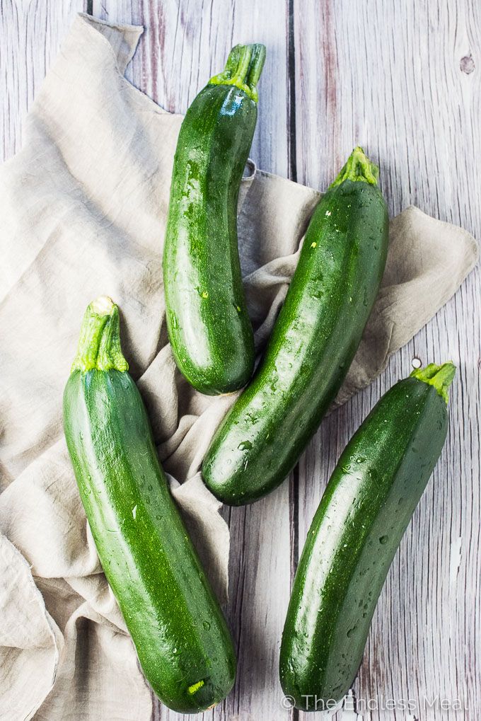 four green cucumbers sitting on top of a wooden table next to a cloth