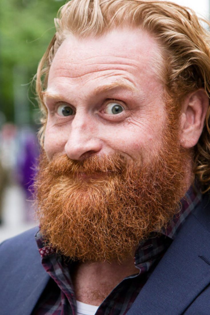 a man with a red beard and long hair wearing a blue jacket looking at the camera