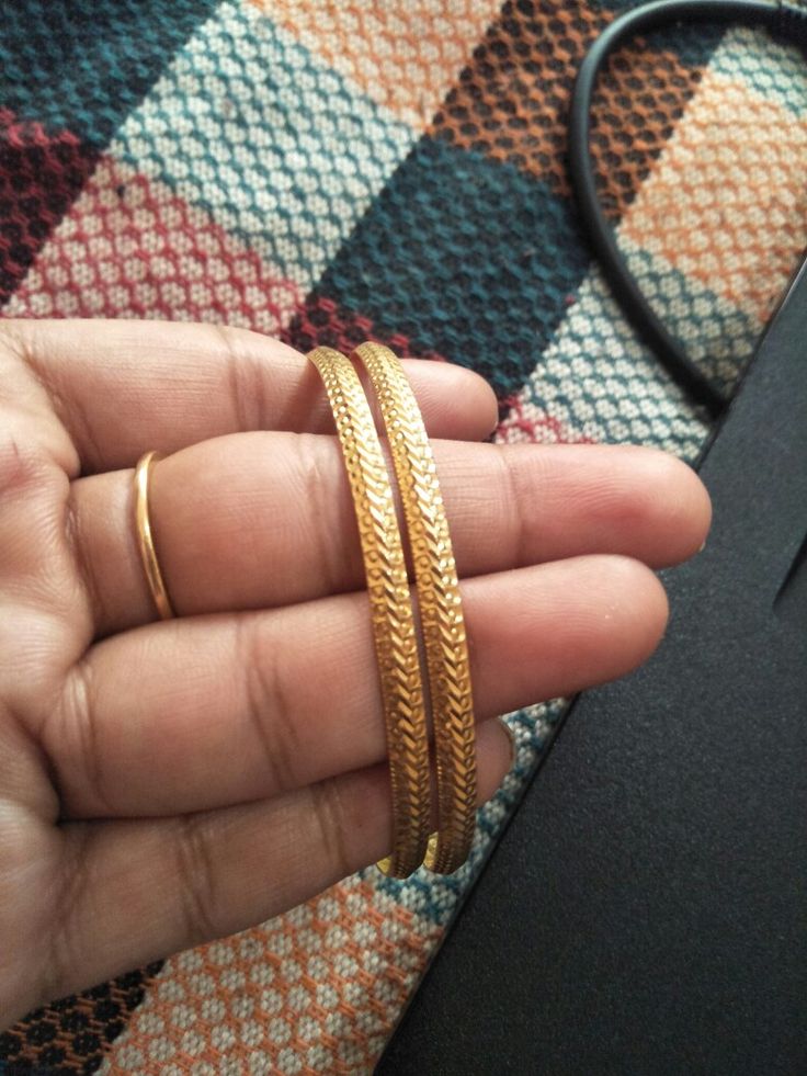 a person holding two gold colored bangles in their hand on a checkered cloth