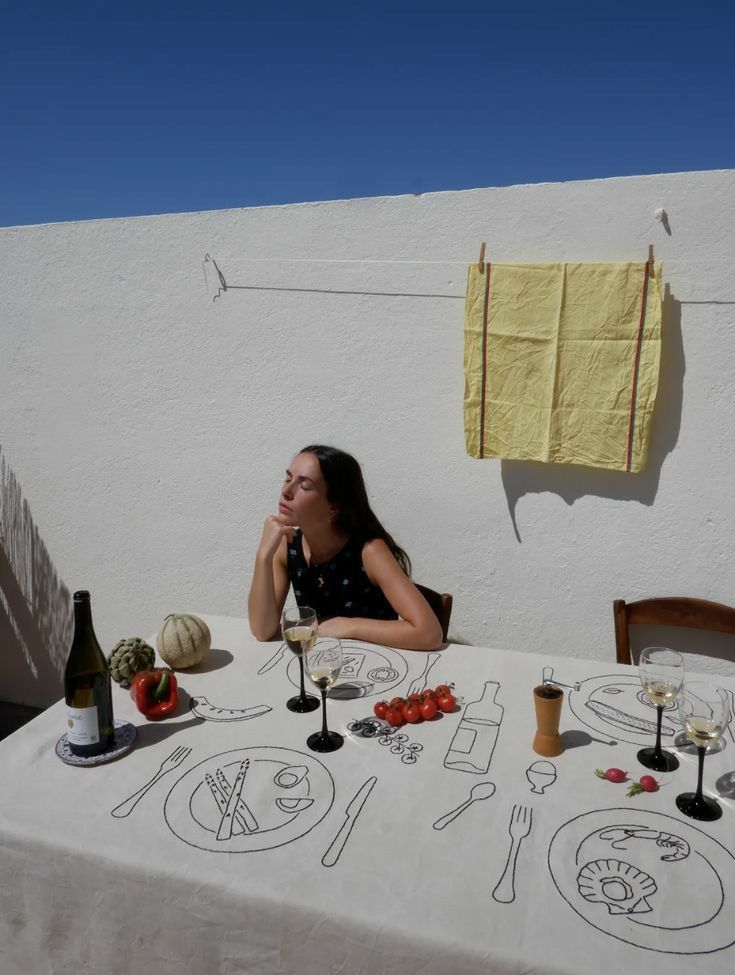 a woman sitting at a table with food and wine