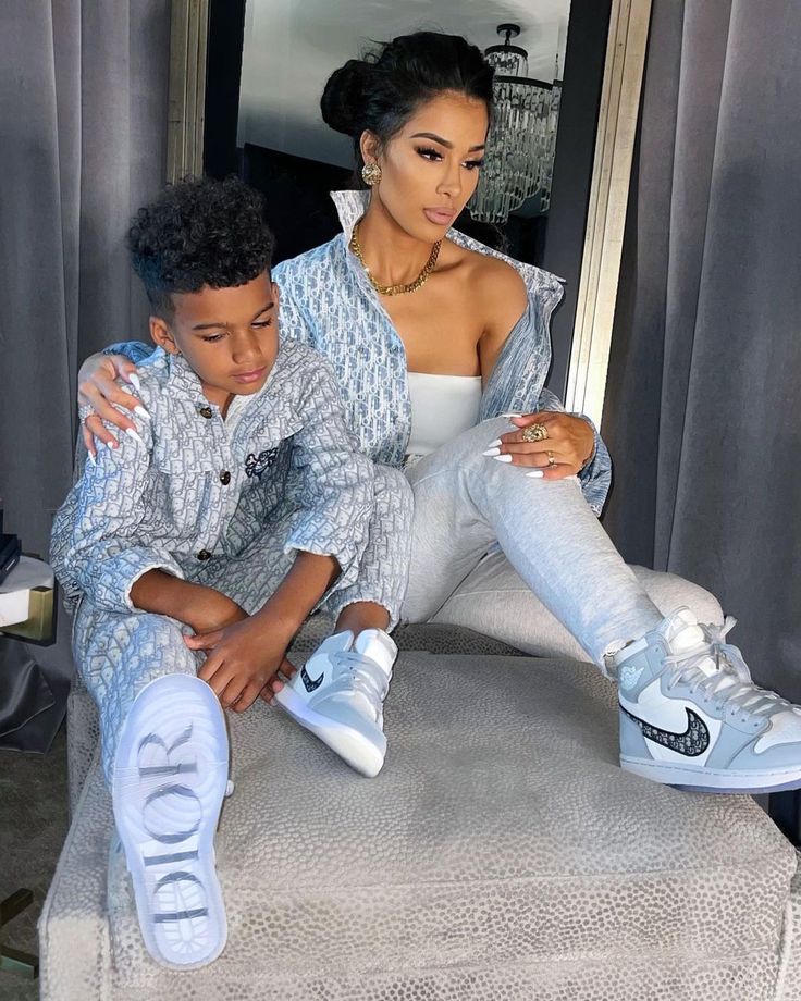 a woman sitting on top of a bed next to a young boy wearing sneakers and jeans