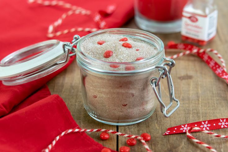 a glass jar filled with red and white stuff on top of a wooden table next to other items