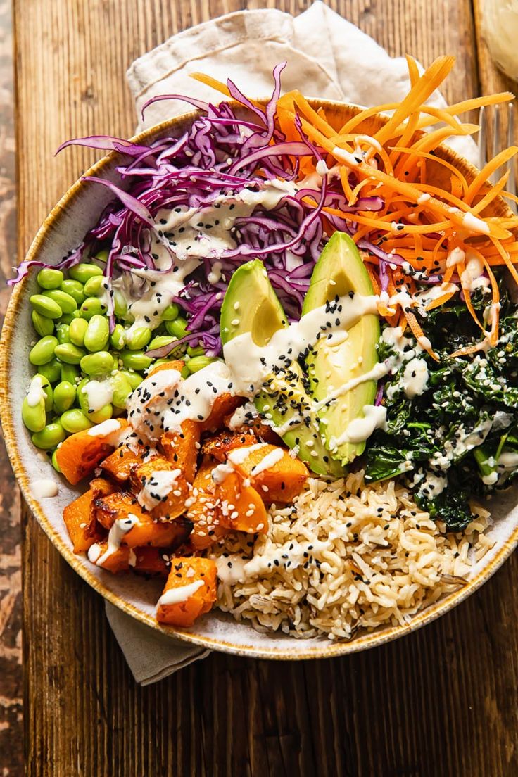 a bowl filled with rice, carrots, avocado, and other veggies