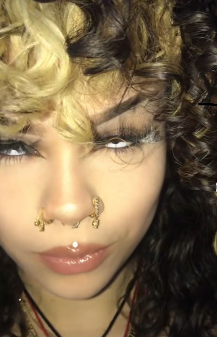 a close up of a person with curly hair and piercings on her nose,