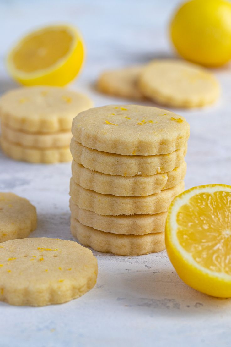 a stack of lemon shortbread cookies next to sliced lemons on a white surface