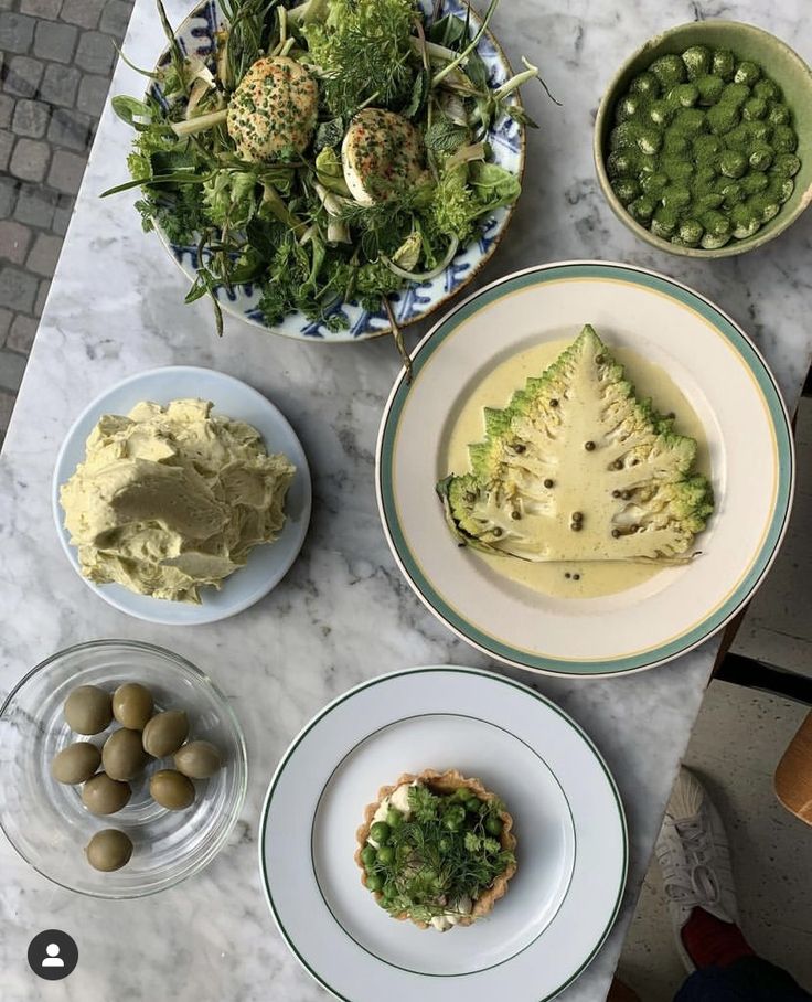 several plates with food on them sitting on a marble counter top next to bowls of vegetables and dips