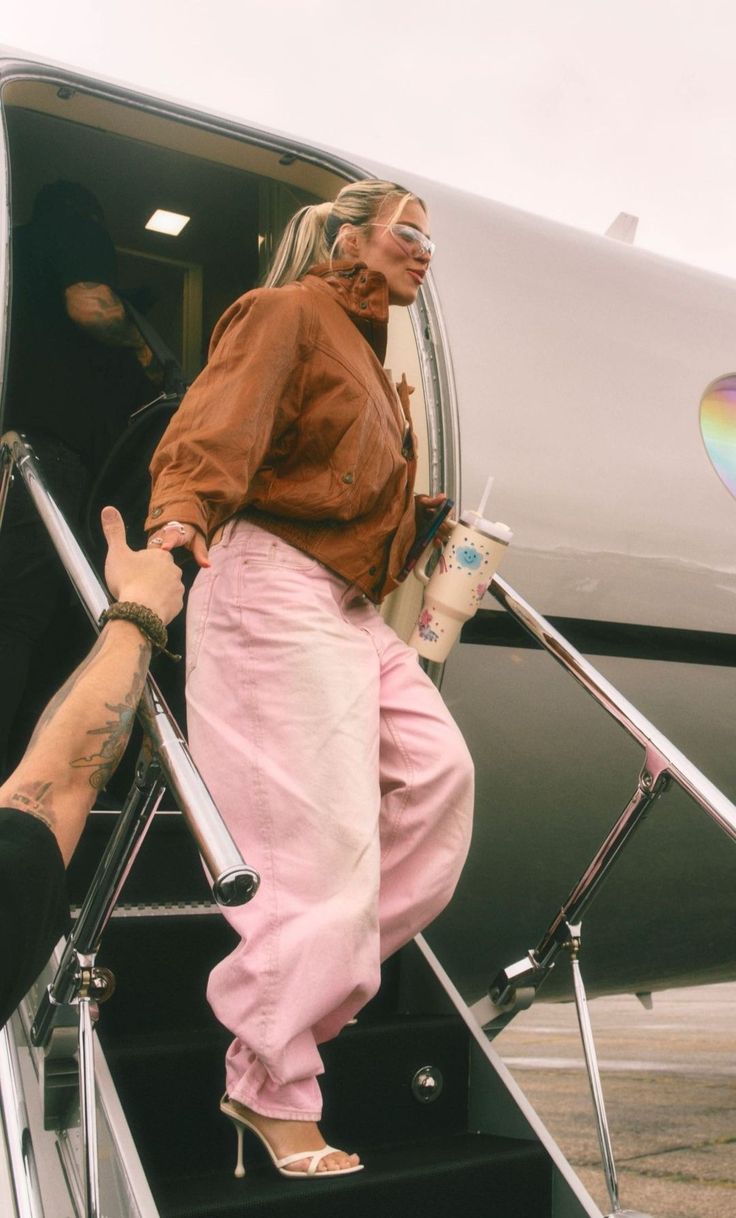 a woman in pink pants stepping off an airplane with her hand on the steps and another person standing next to her