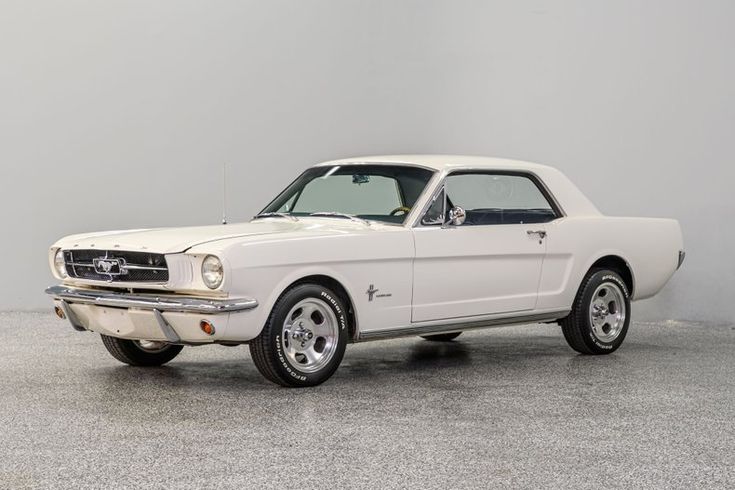 an old white mustang sitting on top of a cement floor next to a gray wall