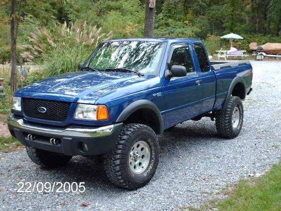 a blue pick up truck parked on top of a gravel road in front of trees