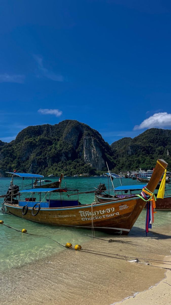 two boats on the beach with mountains in the backgrouds and clear blue water