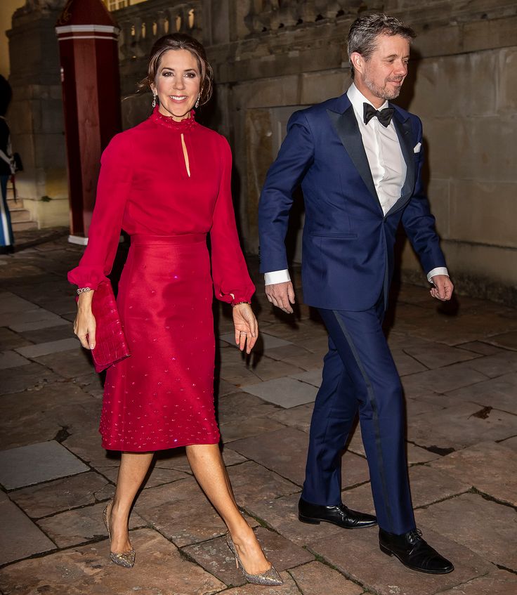 a woman in a red dress walking next to a man in a blue suit