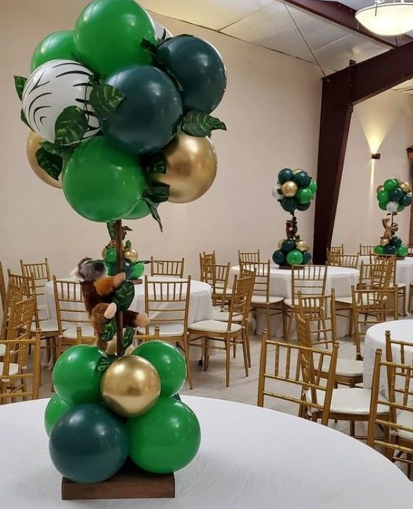 a table topped with lots of green and gold balloon decorations on top of white clothed tables