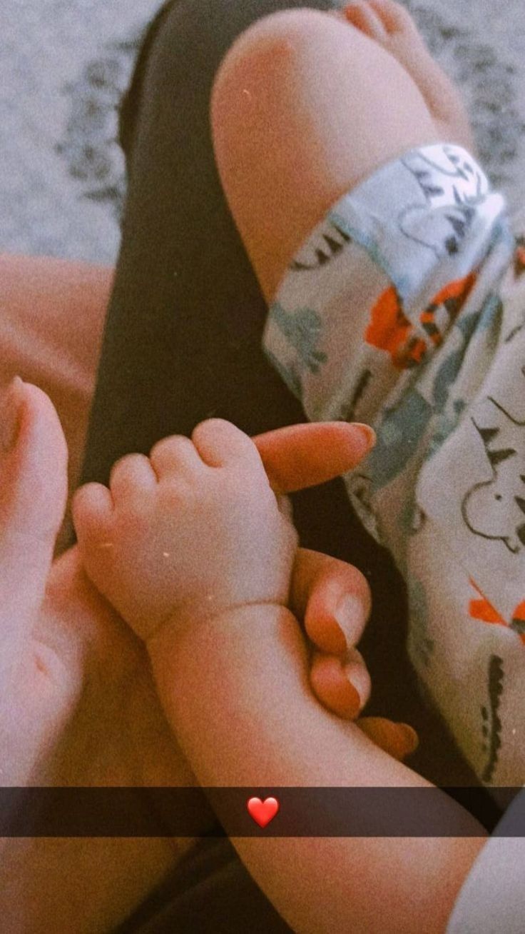 a woman holding a baby's hand while laying on top of her stomach with a red heart in the middle