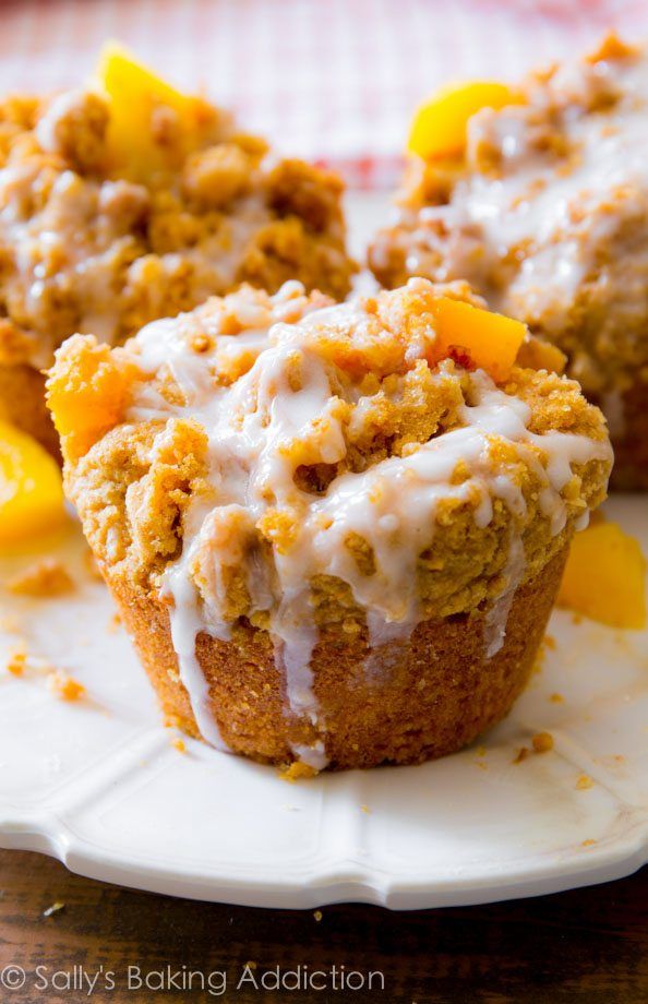 a muffin on a plate with frosting and peaches around it, ready to be eaten