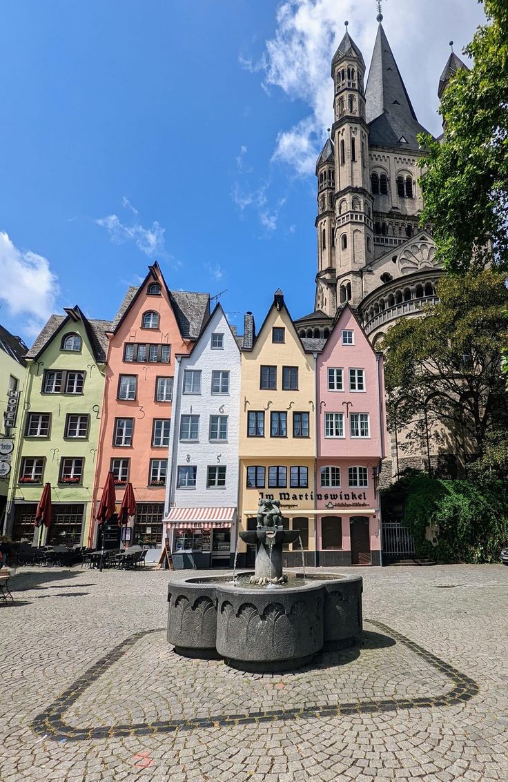 several colorful buildings with a clock tower in the background and a fountain in the foreground