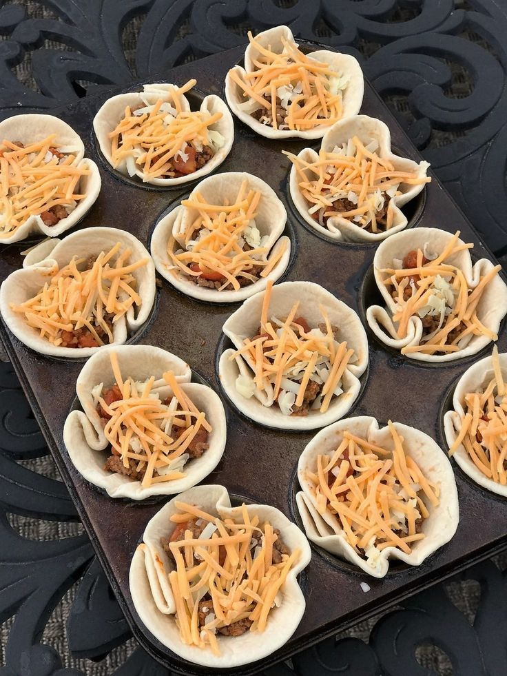 nine small bowls filled with cheese on top of a metal tray in front of a black wall