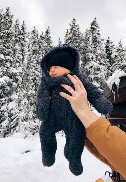 a person holding a baby in the air with snow on the ground and trees behind them