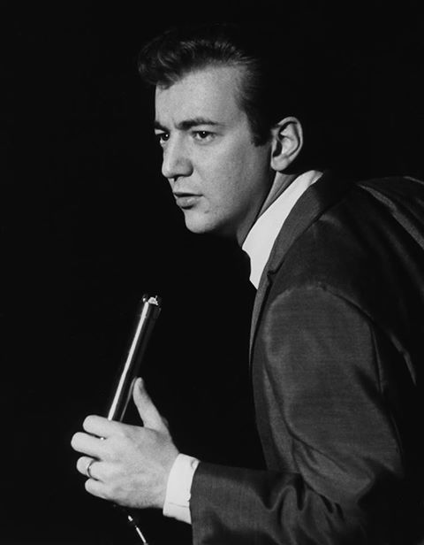 a black and white photo of a man in a suit holding a microphone with his right hand