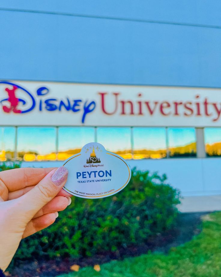 a person holding up a disney university sticker in front of a building with the logo on it