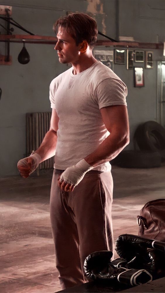 a man in white shirt and brown pants standing next to a bag with boxing gloves on it