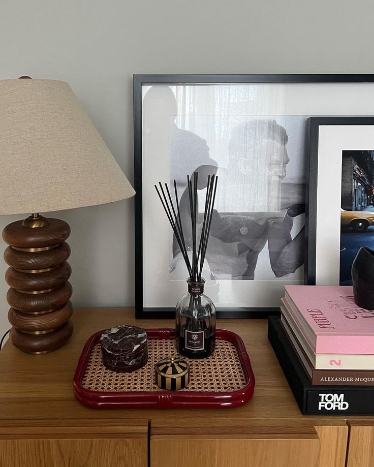 a lamp and some books on a wooden table next to a framed photo with a man's face