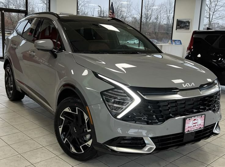 the front end of a silver suv in a showroom with other cars behind it